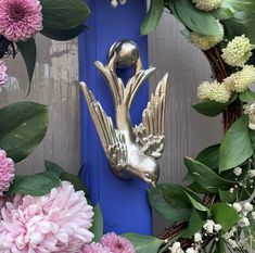 a blue door with flowers and a metal bird on it's front handle, surrounded by greenery