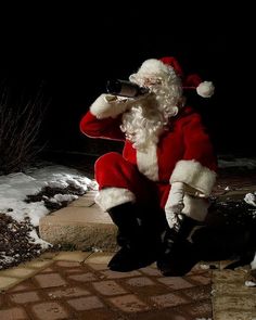 a man dressed as santa claus drinking from a wine glass while sitting on a brick walkway