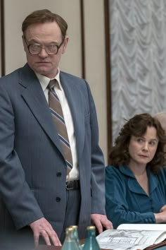 a man in a suit and tie standing next to a woman sitting at a table