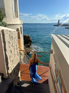 a woman in a blue dress is walking down some stairs near the ocean and boats