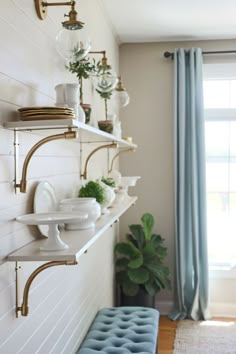 a room with some shelves and plants on the wall next to a blue bench in front of a window