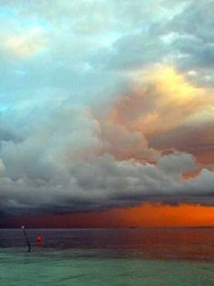 the sky is filled with clouds as it sits over the ocean in front of an orange and blue sunset