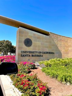 the university of california santa barbara sign in front of flowers and bushes on a sunny day