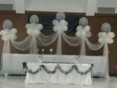 balloons are hanging from the ceiling above a table with white linens and black chairs