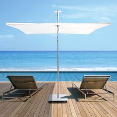 two lawn chairs sitting on top of a wooden deck next to an umbrella over the ocean