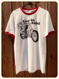 a t - shirt that says keep on riding hanging on a wooden wall next to a hanger