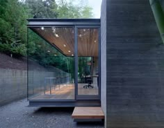 a glass walled room with a wooden bench in the foreground and trees in the background