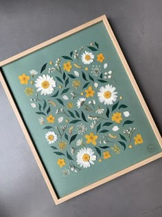 a painting with yellow and white flowers on a green background is displayed in a wooden frame