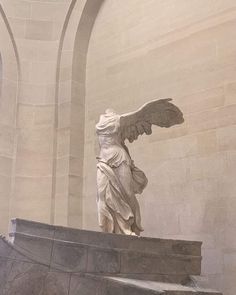 an angel statue on top of a stone bench in a building with arches and windows