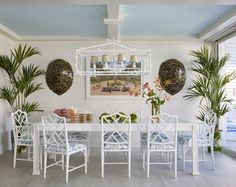 a white dining room table with chairs and potted plants