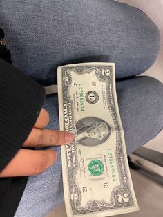 a person is sitting down and holding a one dollar bill