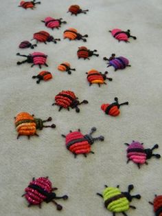 small knitted bugs sitting on top of a white sheet covered in beads and thread