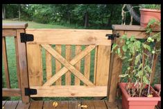 a wooden gate on top of a wooden deck next to potted plants and trees