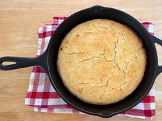 a cast iron skillet on a red and white checkered cloth with a baked bread in it