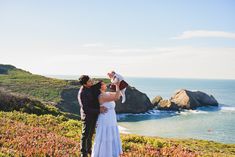 a bride and groom standing on top of a hill next to the ocean