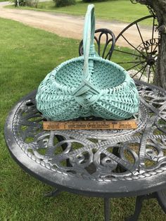 a basket sitting on top of a metal table next to a tree in the grass