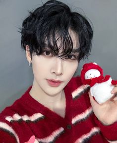 a man holding a stuffed animal in his hand and wearing a red striped shirt with black hair