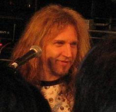 a man with long hair standing in front of a microphone