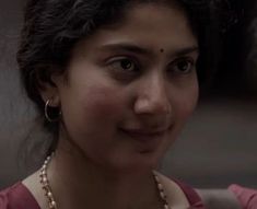 a woman in a pink shirt and pearl necklace looking at the camera with an intense look on her face