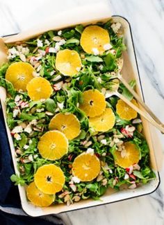 a salad with oranges and nuts in a white dish on a marble counter top