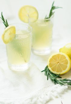 two glasses filled with lemonade and rosemary garnish on top of a white cloth