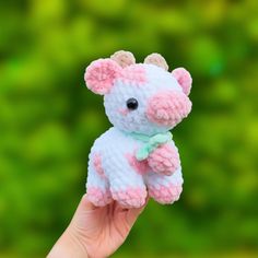 a hand holding a small crocheted pink and white teddy bear in front of a green background