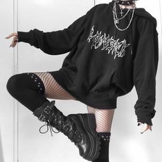 a woman in black is posing with her legs spread out, wearing boots and a hoodie