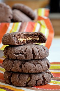 a stack of chocolate cookies sitting on top of a striped table cloth next to a bowl of cookies