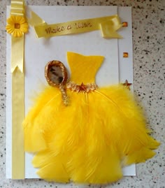 a card with a yellow dress on it and a gold brooch in the middle