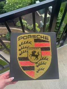 someone is holding up a porsche emblem on their balcony railing, with trees and bushes in the background