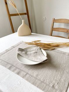 a table with a white plate and some wheat stalks on it, next to a vase