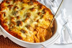 a casserole dish with meat and cheese in it on a cloth next to a fork