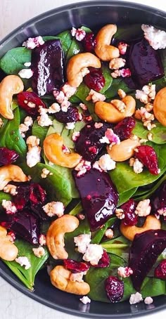 a salad with beets, walnuts and spinach in a black bowl on a white table