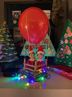 two elfs riding in a hot air balloon with christmas trees and decorations around them