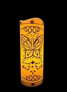 a lit candle with an intricately designed design on the front and sides, against a black background