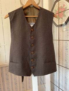 This classic vest is made from 100 per cent wool in a small houndstooth pattern, in brown and black with a bit of white running throughout. The vest has the original buttons and two front pockets, and is fully lined with brown silky lining. From Club International by Tip Top Tailors; marked size large. The measurements, taken with the vest lying flat, are: shoulder to shoulder, 17 inches; armpit to armpit, 22 inches; length, 23 inches in front and 23 inches in back; bottom edge, 23 inches. In very good condition. Wool Business Vest For Fall, Wool Vest For Business In Fall, Tweed Business Vest For Fall, Business Tweed Vest For Fall, Fall Business Tweed Vest, Brown Houndstooth Tweed Jacket For Business, Classic Tailored Vest For Fall, Classic Business Vest For Fall, Brown Business Vest For Fall