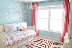 a bedroom decorated in blue and pink with a tree painted on the wall