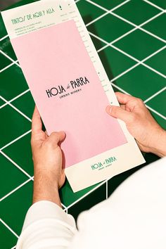 a person holding a pink book on top of a green tiled floor with white tiles