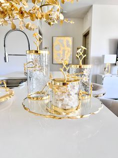 three glass containers with gold decorations on top of a white counter in a living room