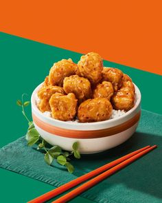 a bowl filled with fried food next to chopsticks on a green and orange tablecloth