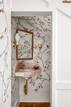 a bathroom with floral wallpaper and gold faucet, marble sink and mirror