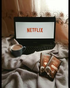 a laptop computer sitting on top of a bed next to three chocolate bars and a cup of coffee