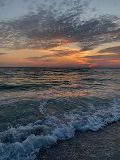 the sun is setting over the ocean with waves crashing on the shore and clouds in the sky