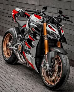 a red and silver motorcycle parked next to a brick wall