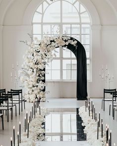 an aisle with white flowers and candles is shown in front of a large arched window