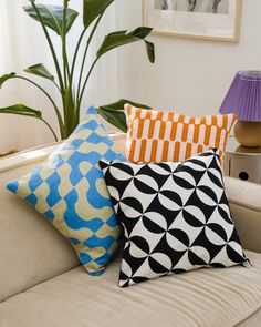 four different colored pillows sitting on top of a white couch next to a green plant