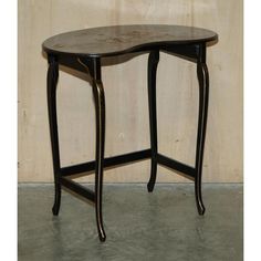 an oval shaped table with black legs and a wooden top, against a beige wall