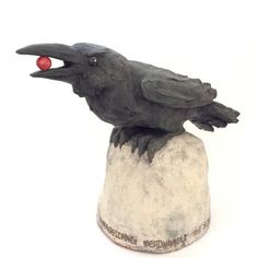 a statue of a black bird sitting on top of a white rock with a red ball in its beak