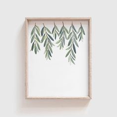 a white frame with green leaves hanging on it's side, against a wall