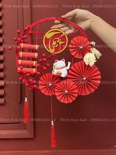 a hand holding a red paper fan with chinese characters on it and flowers in the background